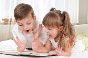 Lovely children - brother and sister, reading a book, on the bed