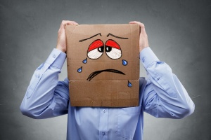 Businessman with cardboard box on his head showing a crying sad